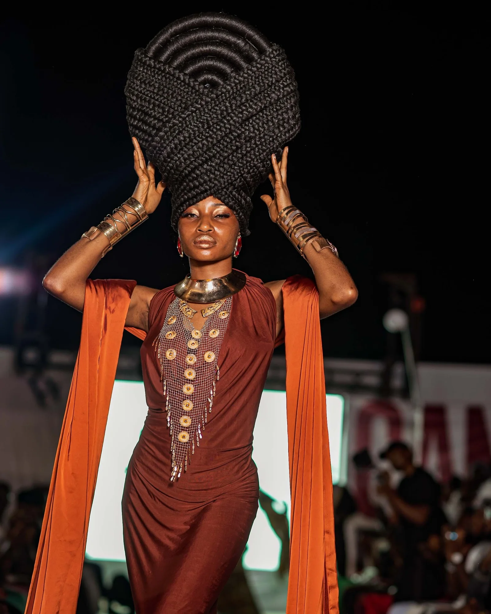 Model in a sculpted headpiece, brown gown and burnt-orange cape on the CAMFFEST 2026 runway